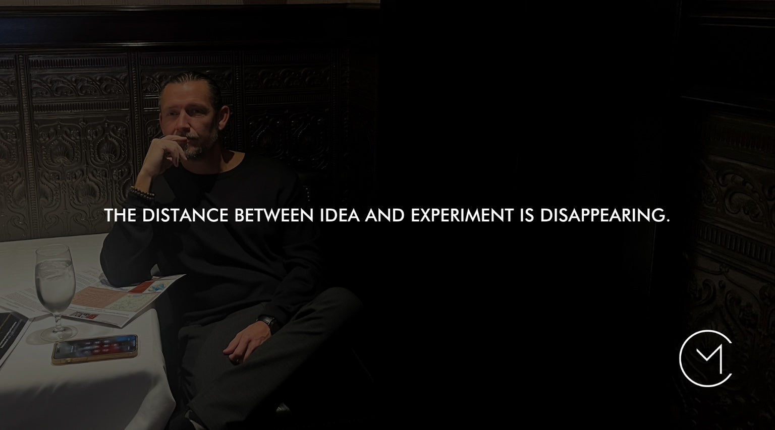 A man sits thoughtfully at a table, illustrating how AI is shrinking the distance between an idea and a practical experiment.