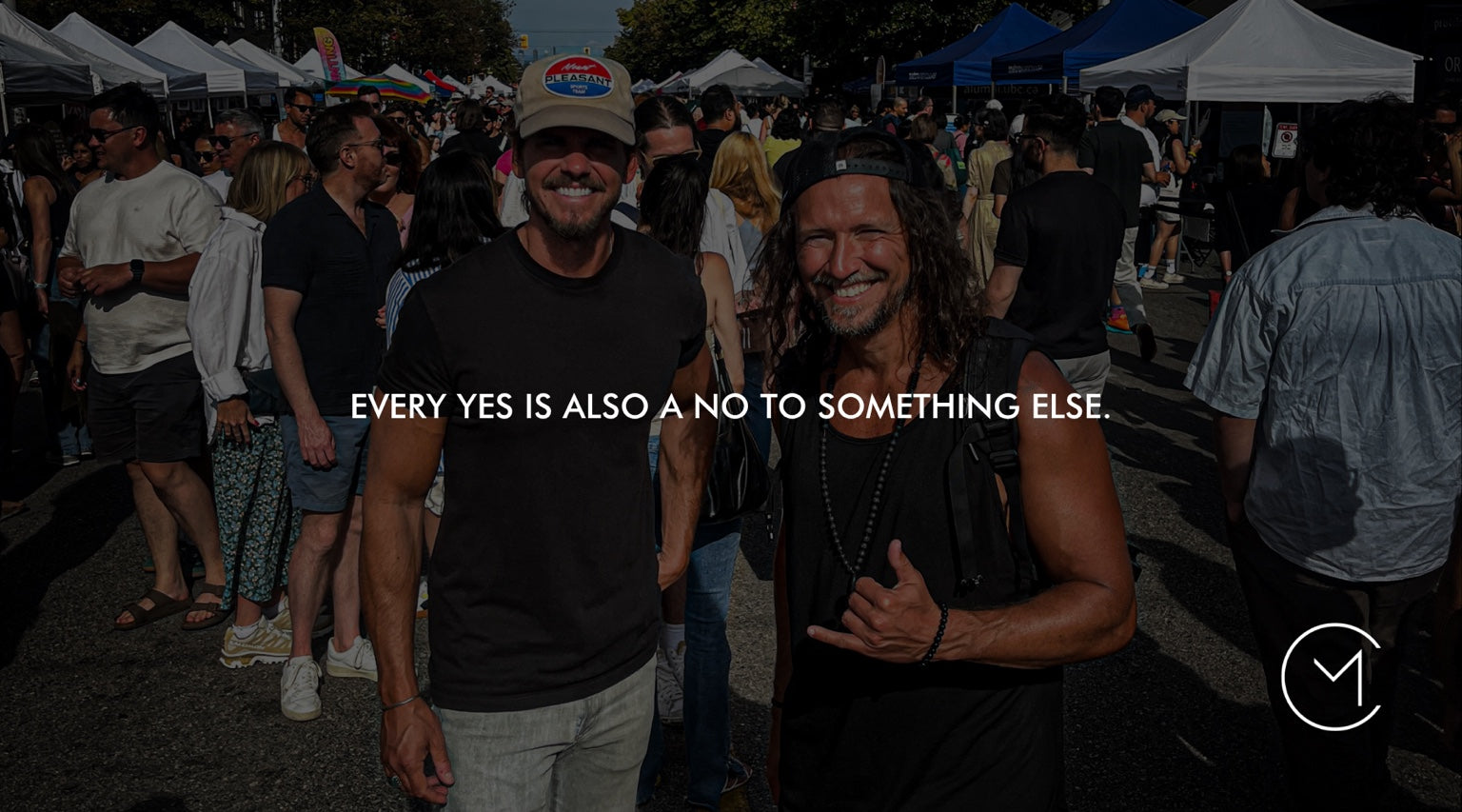 Two men smile together at a busy outdoor event, illustrating intentional choices, relationships and what we choose to say yes to.