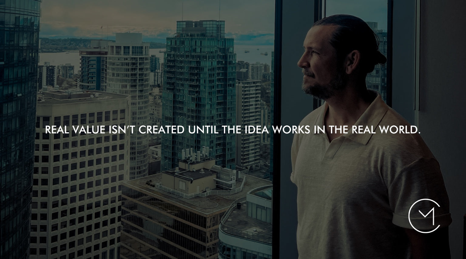 A man looks over a city from a high-rise window, illustrating commercialization and the process of making an idea work in the real world.