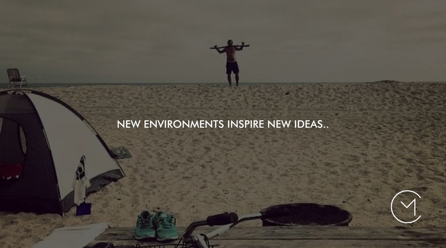 A man stands on a sandy beach near a tent and surfboard, illustrating how new environments can inspire new ideas and perspective.