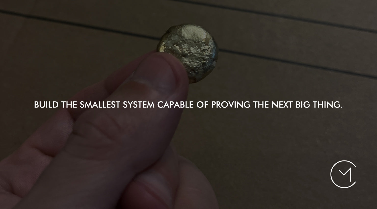 A hand holds a small metallic sphere, illustrating the venture-building principle of creating the smallest system capable of proving the next thing.